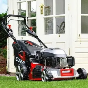 the Cobra MX484SPCE Electric Start Lawn Mower parked outside a white summerhouse