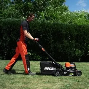 a man wearing an orange and black tradesman's uniform, mowing a lawn with the ECHO DLM-5100SP Cordless Lawn Mower