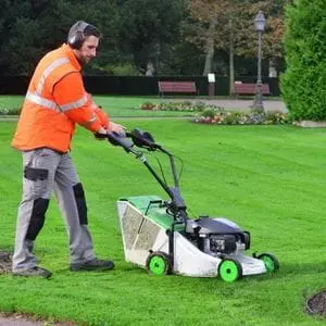 a man wearing ear defenders and a high-visibility orange jacket, cutting a lawn using the Etesia Pro 46 PHE3 Petrol Lawnmower
