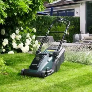 the Hayter Hawk 43 Cordless Lawnmower parked on a striped lawn, in an attractive garden, near a white-walled house