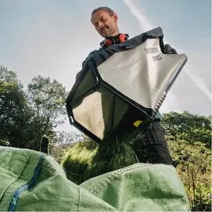 a man dropping grass clippings from a Honda grass bag into a large, green tarpaulin sack