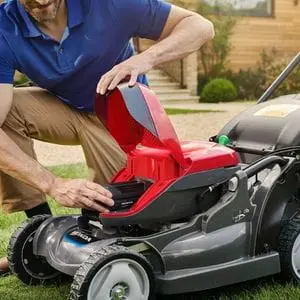 a man crouched down, inserting a battery into a Honda cordless lawn mower