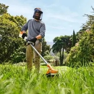 a man cutting an overgrown lawn using the Husqvarna LC 251iS Grass Trimmer