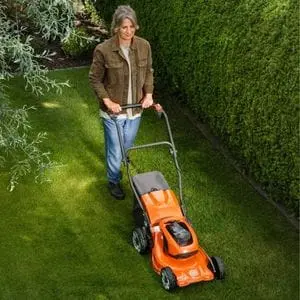 a woman mowing a lawn in a neatly manicured garden, using a Husqvarna LC137i Cordless Mower