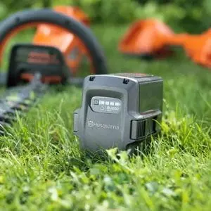 a Husqvarna lithium-ion battery on a lawn, next to two cordless tools
