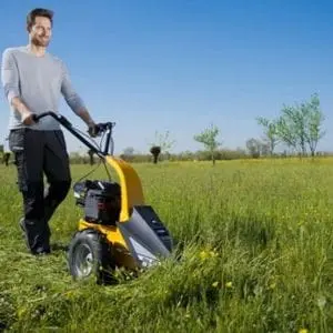 a man cutting grass in a wide-open field, using the STIGA Silex 87G Petrol Scythe Mower