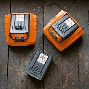 three STIHL batteries, two of which are in chargers, positioned on a wooden table