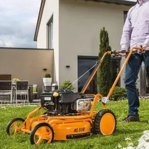 a man cutting the lawn outside of a cream-walled house, using the AS Motor AS510 Pro Clip 4T A Mulching Lawn Mower