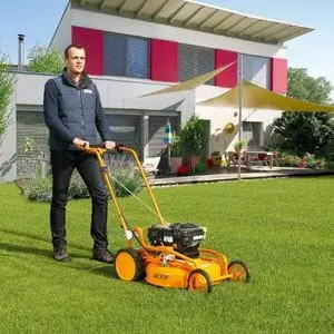 a man using the AS Motor AS510 Pro Clip 4T A Mulching Lawn Mower to maintain an immaculate lawn near a modern house with a pent roof