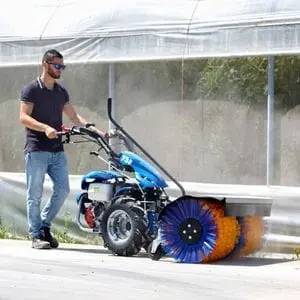 a man cleaning a concrete path using the BCS 738 PowerSafe® 2 Wheel Tractor with a brush attachment
