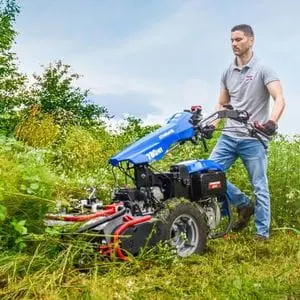 a man operating the BCS 780 HY StarGate Two-Wheel Tractor with Flail Mower Attachment to cut down vegetation