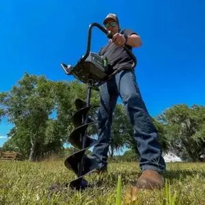 a man wearing sunglasses, drilling a hole in a field, using the EGO PHA7404E Cordless Earth Auger Power Head and ETA0800E Earth Auger Bit