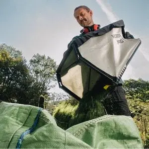 a man emptying the collection bag of a Honda HRH 536 HX Mower into a green tarpaulin sack