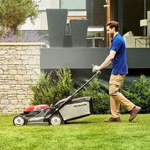 a man using a Honda HRX lawn mower to cut grass outside a house