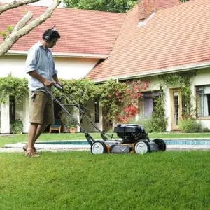 a man wearing shorts and headphones, using a Husqvarna mulching mower to cut grass near a swimming pool