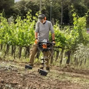a man drilling a hole in the ground in a planting field, in front of some saplings, using the STIHL BT 131 Petrol Earth Auger