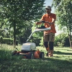 a man mowing a lawn near some trees, using the STIHL RMA 7 RV Cordless Mulching Lawn Mower