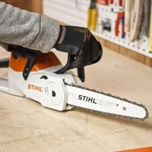 someone wearing black gloves, placing a STIHL chainsaw on a workbench