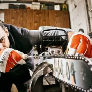 a close up of a man sharpening the chain on a STIHL chainsaw