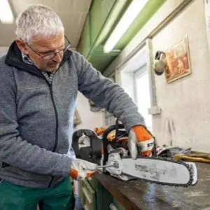 a man with grey hair and glasses, adjusting the tension on a STIHL chainsaw