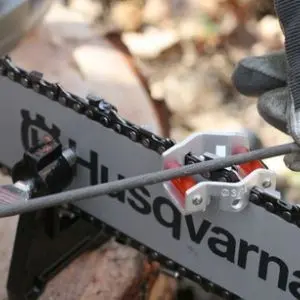 someone using a round file to sharpen the teeth on a Husqvarna chainsaw chain