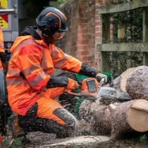 a man knelt on one knee, dressed in orange chainsaw PPE, using the Husqvarna 540i XP® Chainsaw to cut through a log