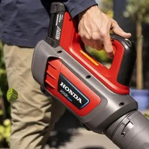 Person holding a red and grey Honda cordless handheld leaf blower.