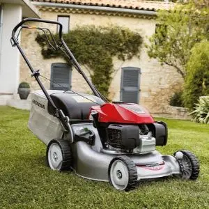 the Honda Izy HRG 466 SK Petrol Lawnmower sat on a lawn, outside a house made of sand-coloured bricks