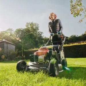 a woman wearing ear defenders, using the Honda HRH 536 HX to mow a lawn