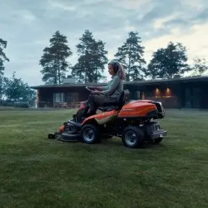 a woman mowing a lawn on an overcast day using the Husqvarna R 216T AWD Out Front Mower