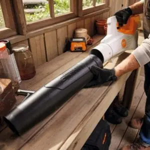Person handling a STIHL BGA 50 cordless leaf blower on a wooden workbench indoors.