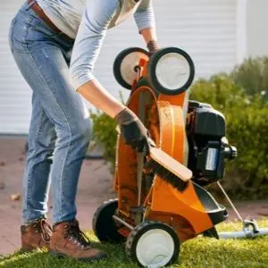 a woman brushing grass clippings off a STIHL lawnmower